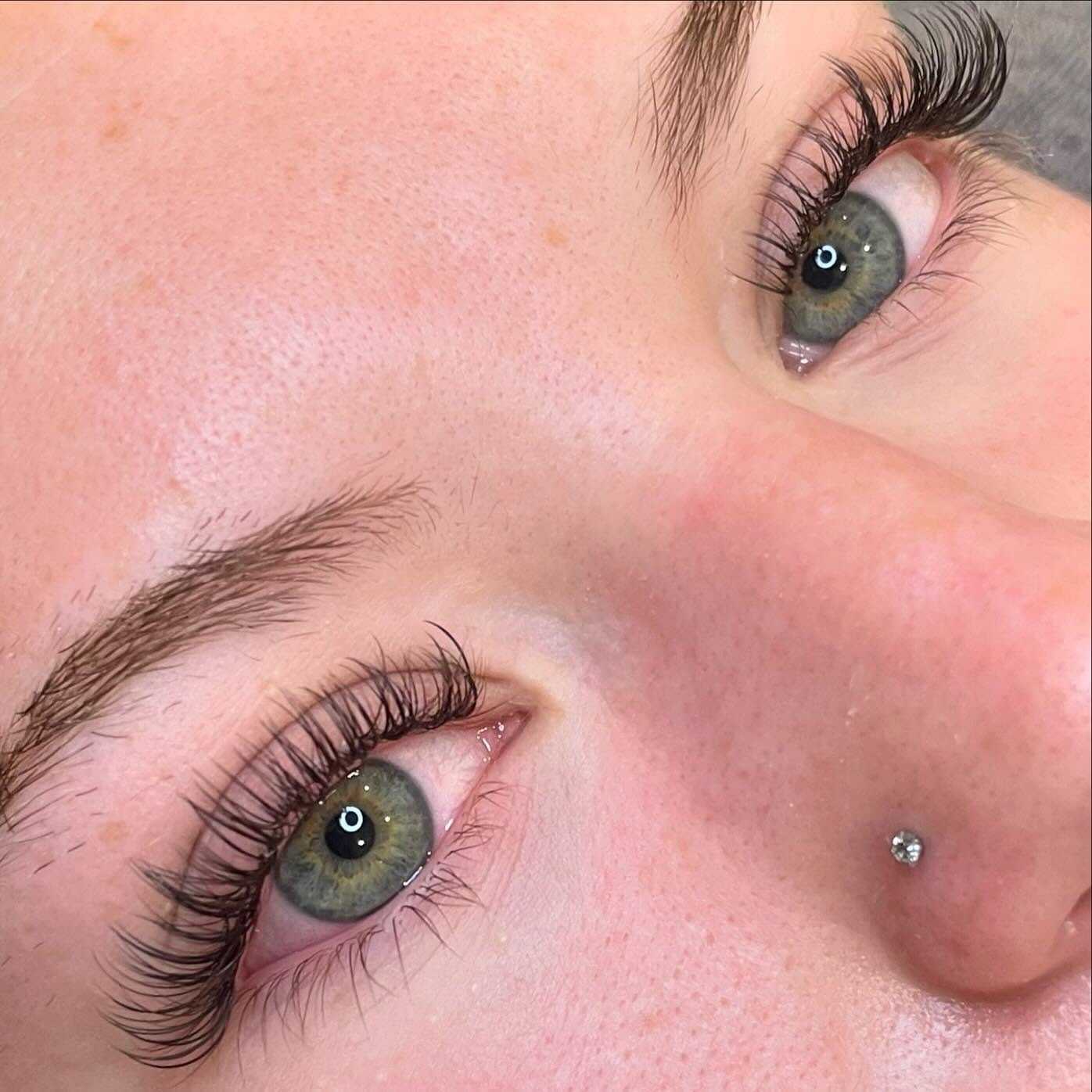 Close-up of a person's eyes with long lashes and a nose piercing.