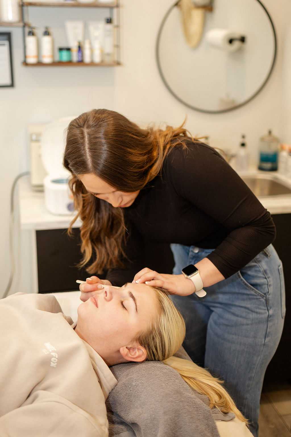 Beautician performing eyebrow treatment on a client in a spa setting.