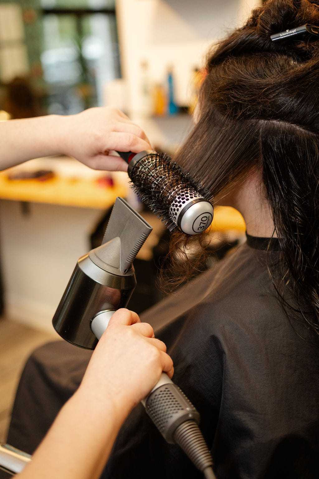Hair being styled with a round brush and hairdryer in a salon.