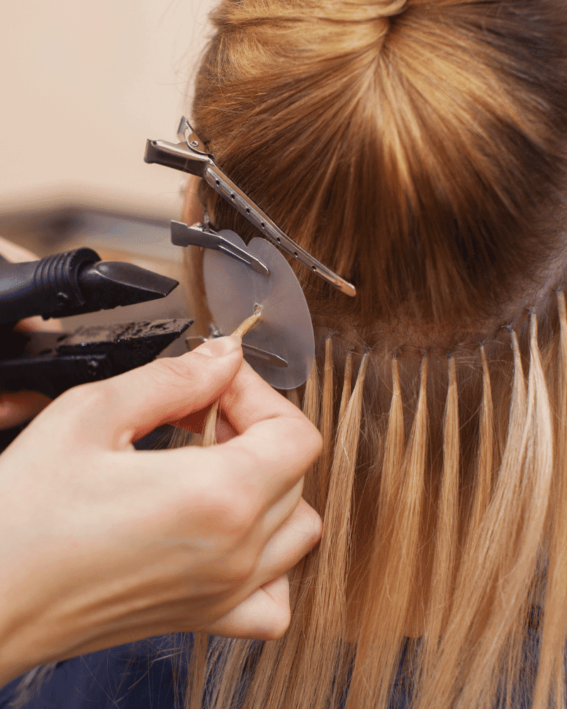 Hair extension being applied by a stylist, using tools to attach strands to natural hair.