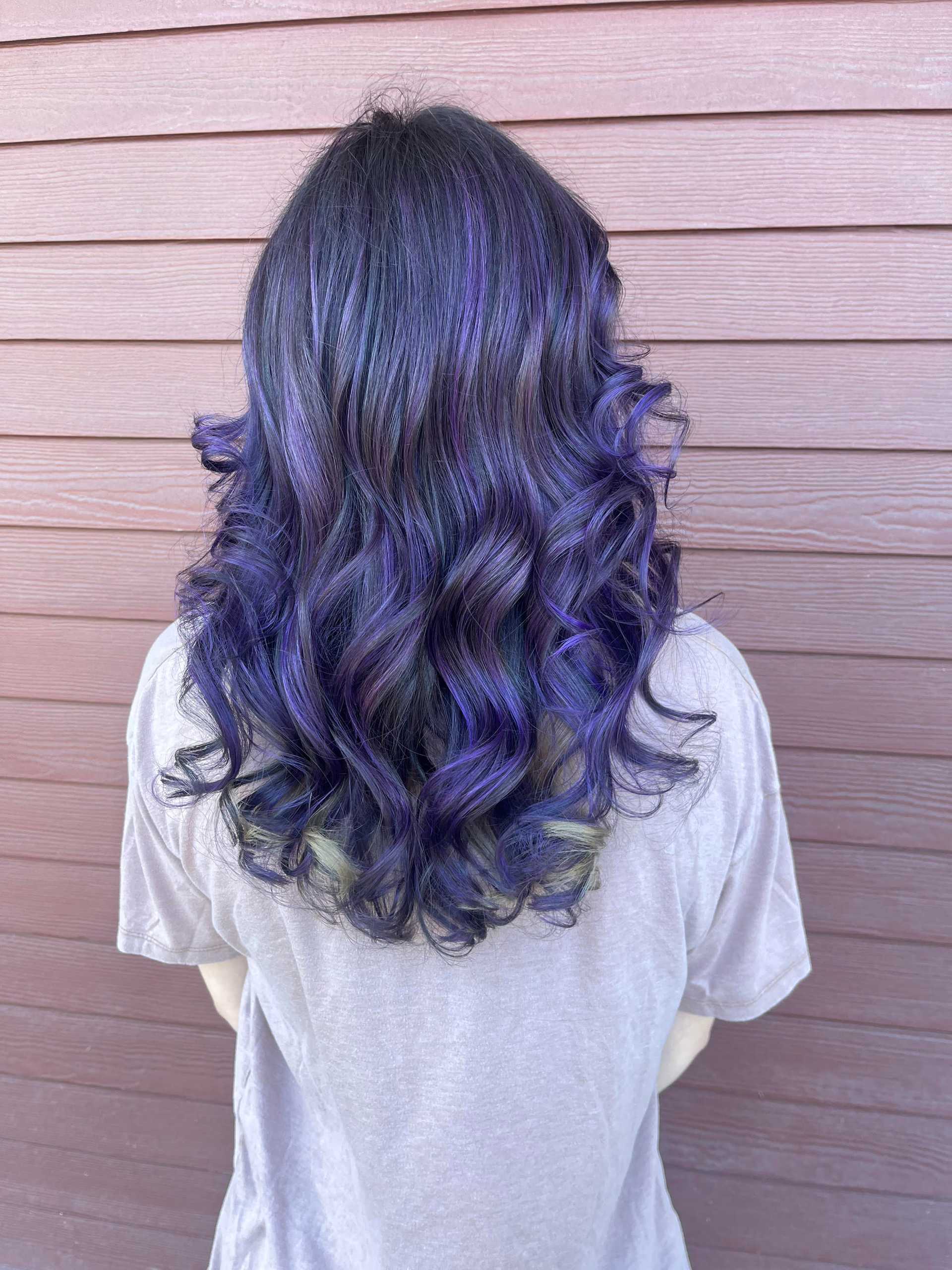 Wavy hair with vibrant purple highlights against a wooden wall background.